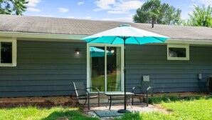 Una veranda coperta con due sedie, un tavolo, una porta scorrevole in vetro e un ombrello verde.