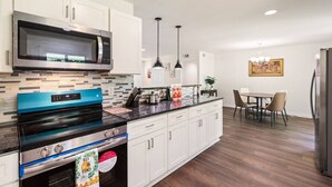 Una cucina moderna con mobili bianchi, un forno blu, un microonde in acciaio inossidabile e un'area pranzo con tavolo e sedie.