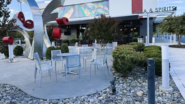 An outdoor seating area with tables and chairs in front of a building with a pizza and spirits sign.