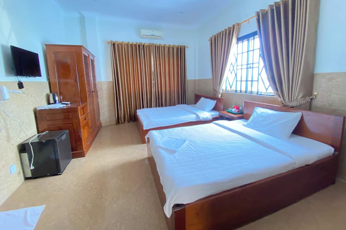 A hotel room with two beds, a wardrobe, a desk with a chair, a television, and a window with curtains.