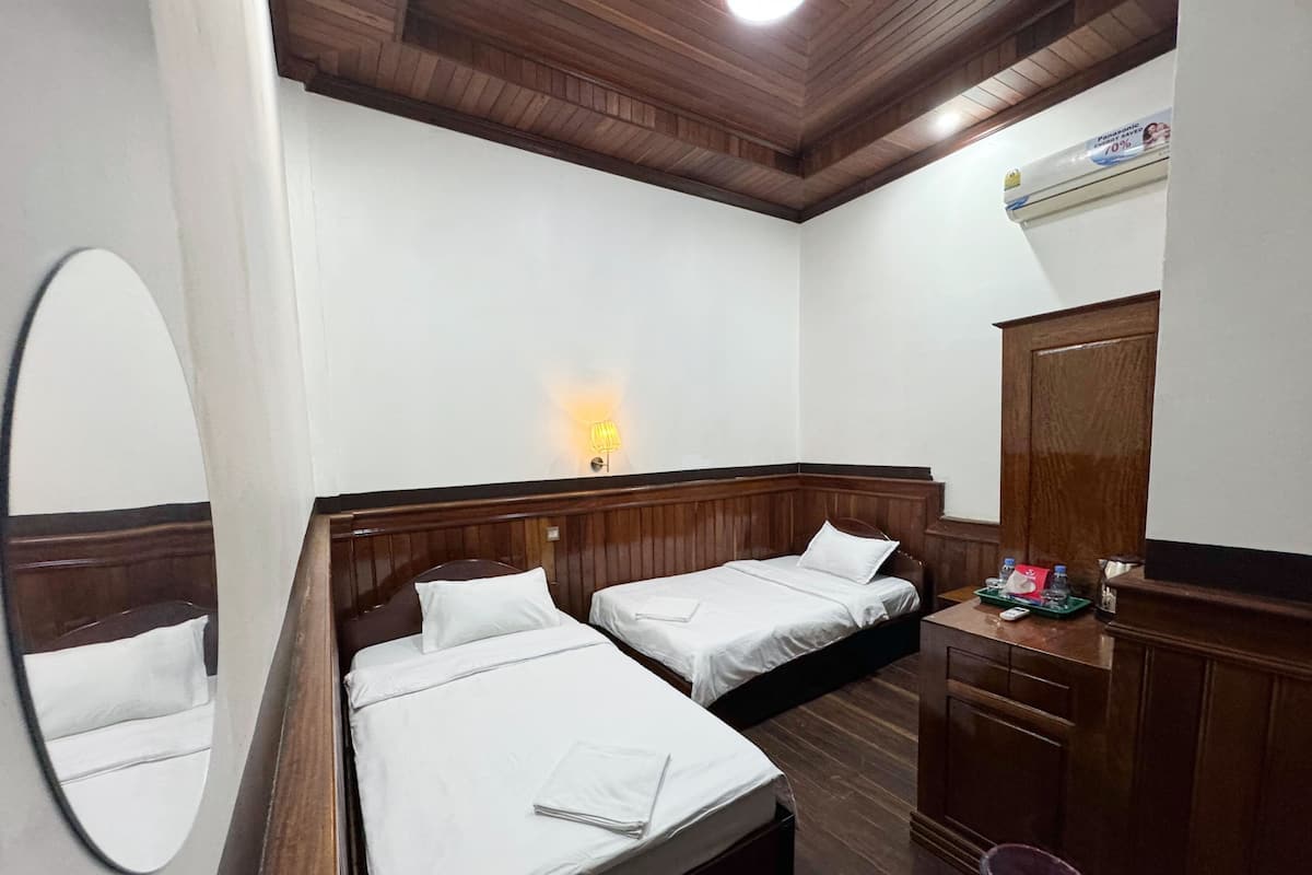 A hotel room with two beds, a wooden ceiling, a wall-mounted air conditioner, a bedside lamp, and a mirror.