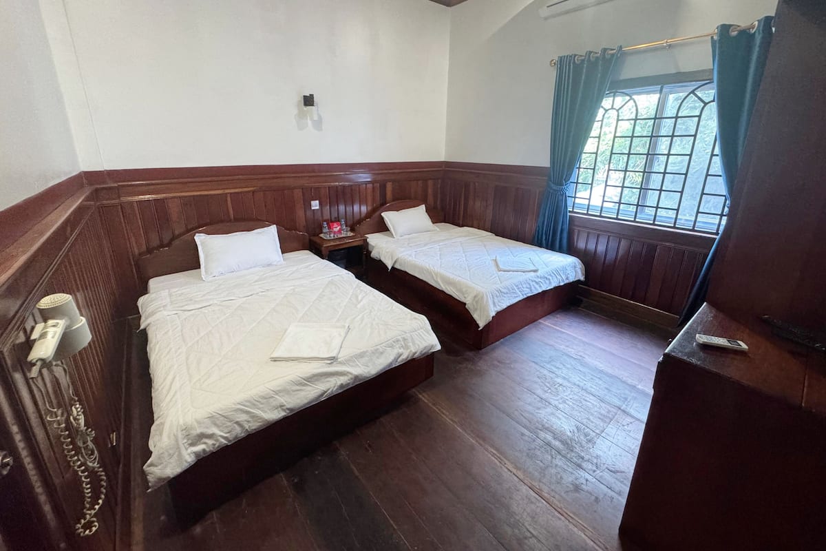 A hotel room with two wooden beds, a small bedside table with a phone, and a window with curtains.