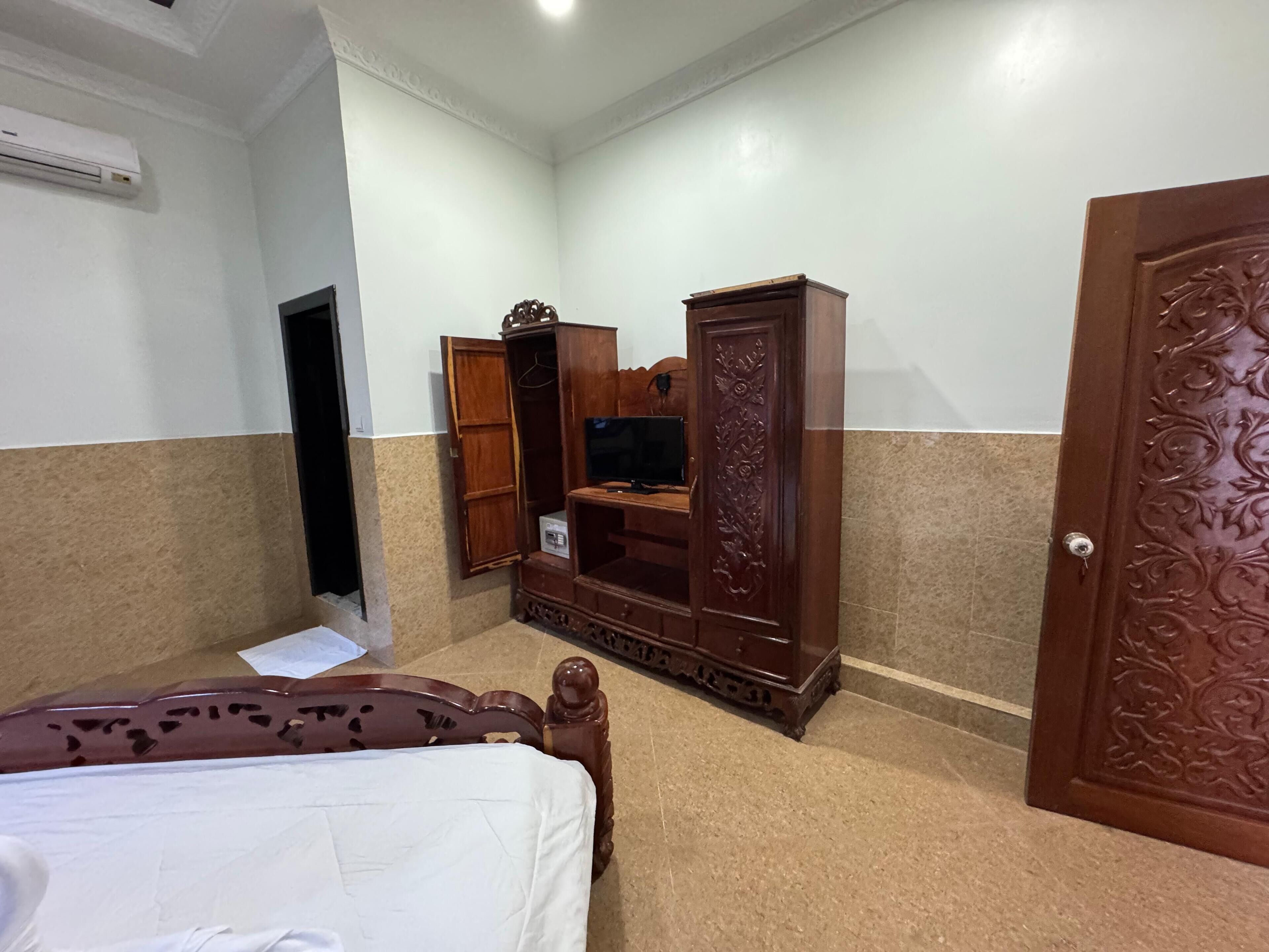 Una habitación de hotel con una cama, un armario de madera, un televisor y una puerta con detalles tallados.