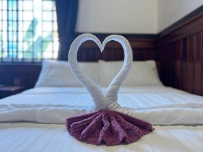 A bed with a white bedspread and a purple towel arranged in a heart shape on the bed. - Angkor Gecko's Inn (Siem Reap)