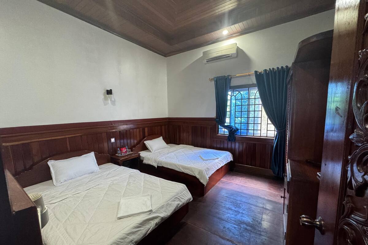 A room with two beds, wooden paneling, a window with curtains, and a door with intricate carvings.