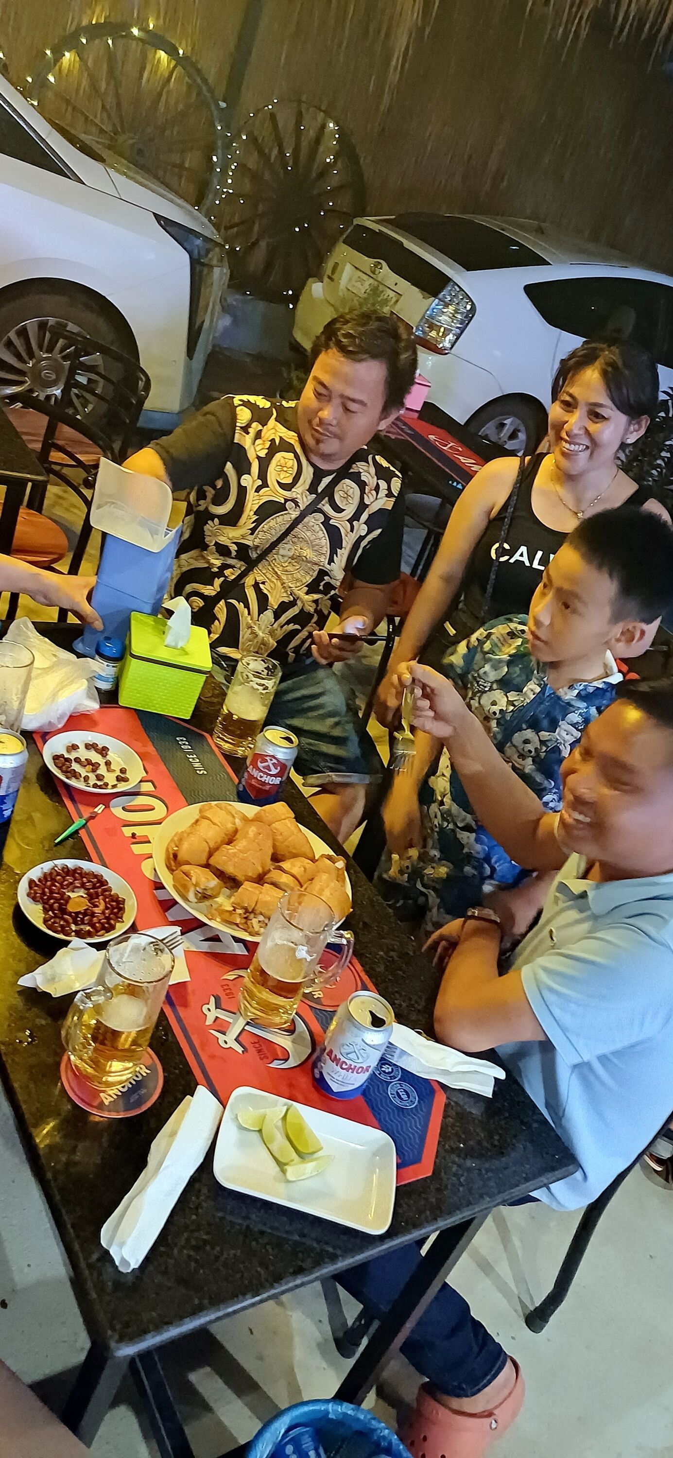 A group of people seated around a table with food, drinks, and a bicycle wheel decoration in the background.