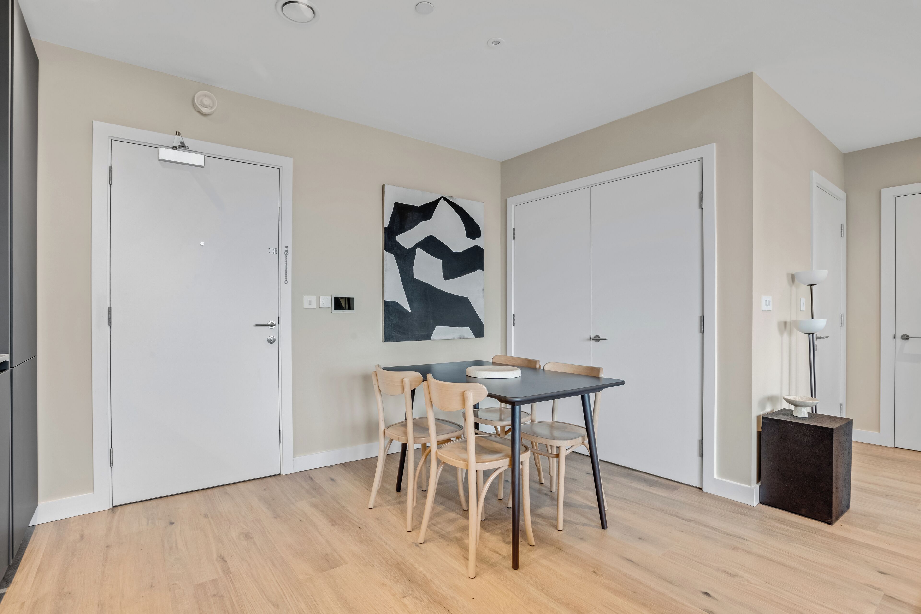 A modern dining area with a table and chairs, a painting on the wall, and two doors.