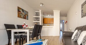 Un salon moderne avec un coin repas, une cuisine à l’arrière-plan et un canapé agrémenté de coussins à motifs.