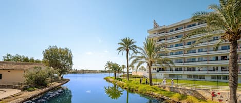 A waterfront property with a calm river, palm trees, and a multi-story building with balconies.