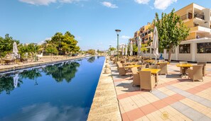 Une terrasse au bord de l’eau avec des sièges extérieurs, une piscine et une rangée de bâtiments dotés de balcons.