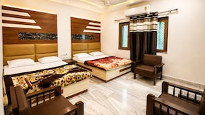 A hotel room with two beds, a sofa, a chair, and a window with curtains. - Hotel Marwari (Agra)