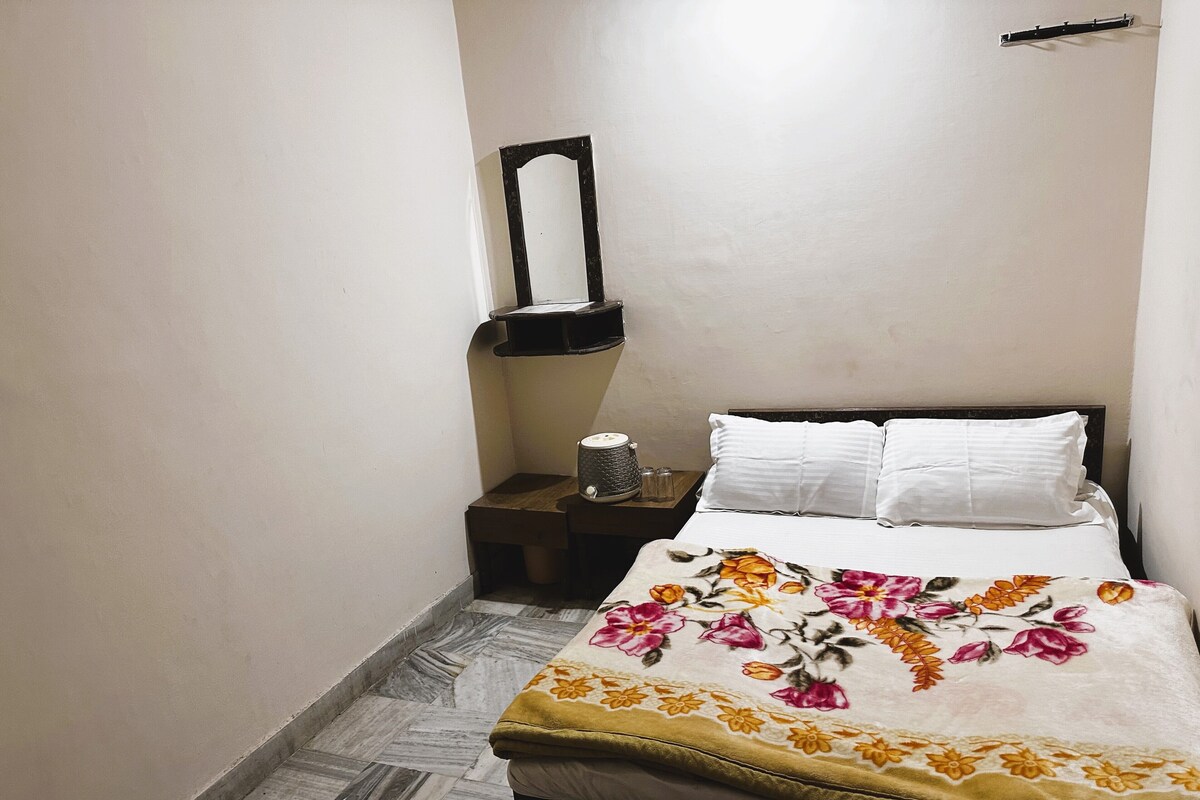 A bedroom with a bed, a nightstand, a mirror, and a tiled floor.
