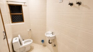 A small bathroom with a toilet, a sink, and a window. - Hotel Marwari (Agra)