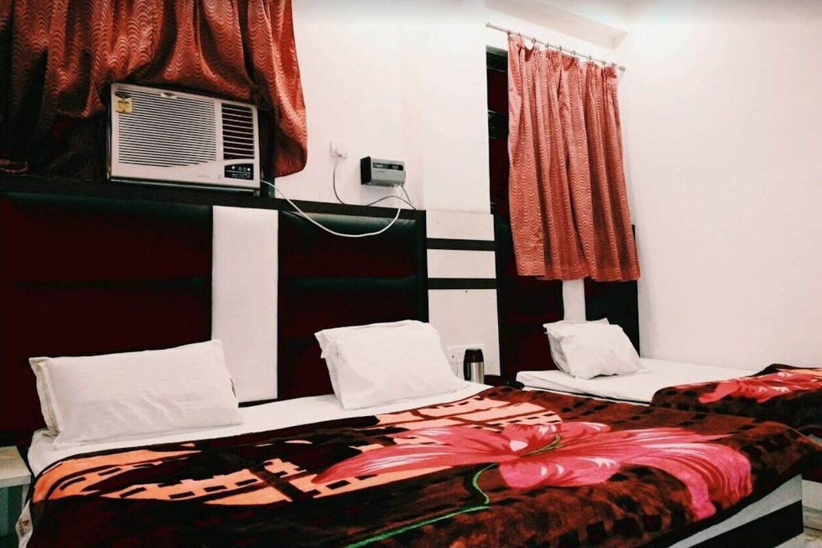 A hotel room with two beds, a large window with curtains, an air conditioning unit, and a wall-mounted heater.