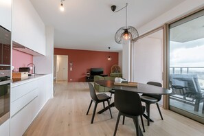 Eine moderne Küche mit weißen Schränken, ein Essbereich mit rundem Tisch und Stühlen sowie eine große Schiebeglastür, die auf einen Balkon führt.