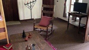 A cozy living room with a wooden rocking chair, a coffee table with decorative items, a television on a stand, and a colorful rug. - w Peaceful 1BR Surrounded by Nature in Huaraz (Yungar)