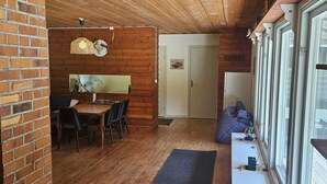 A cozy cabin interior with a wooden dining table, chairs, a small seating area, and a door labeled "MUSTANG".