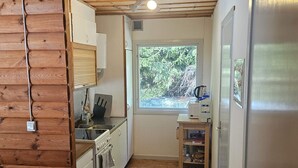 A compact kitchen with wooden cabinets, a sink, a stove, and a window offering a view of greenery outside.
