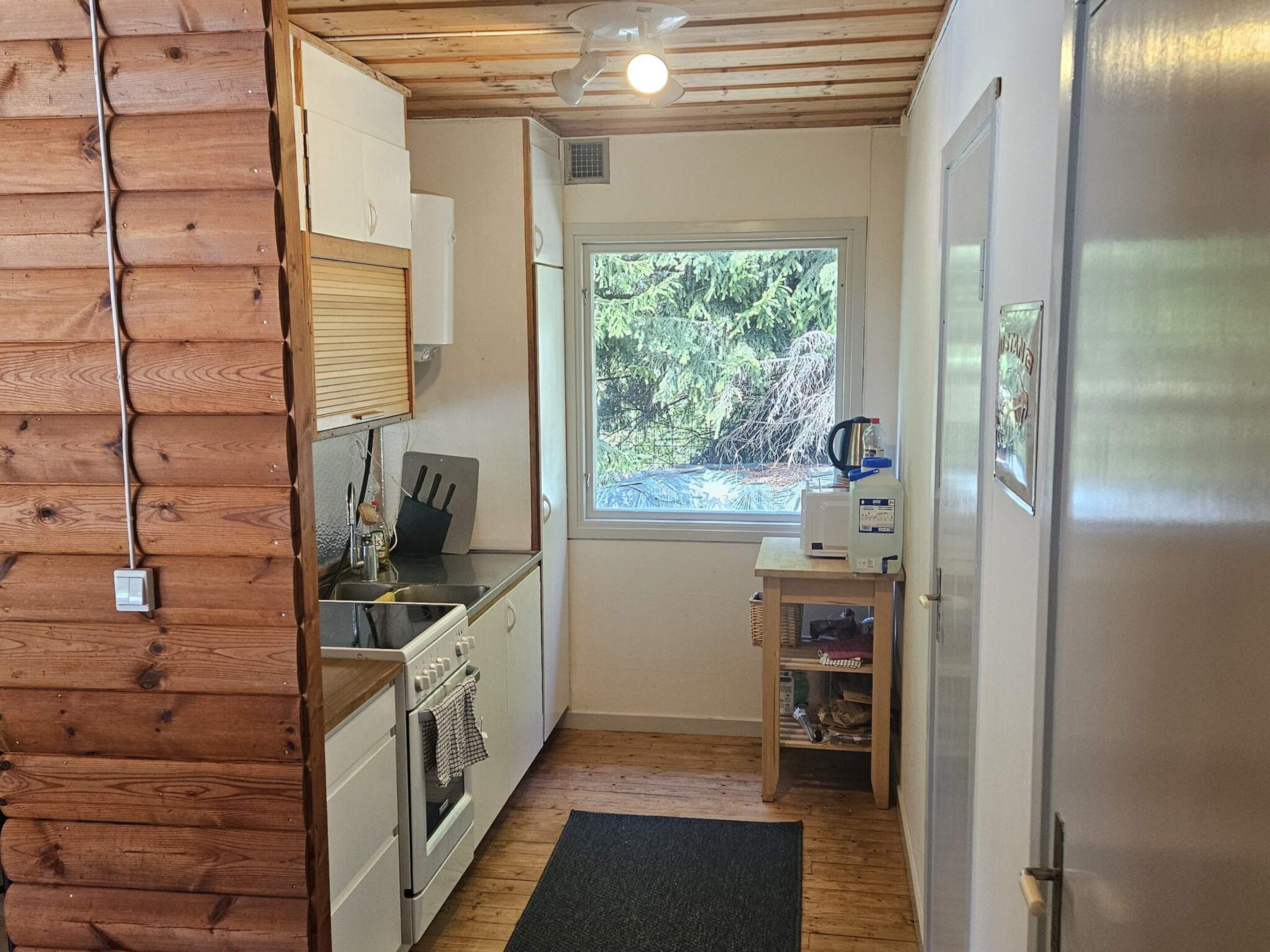 A compact kitchen with wooden cabinets, a sink, a stove, and a window providing a view of greenery outside.