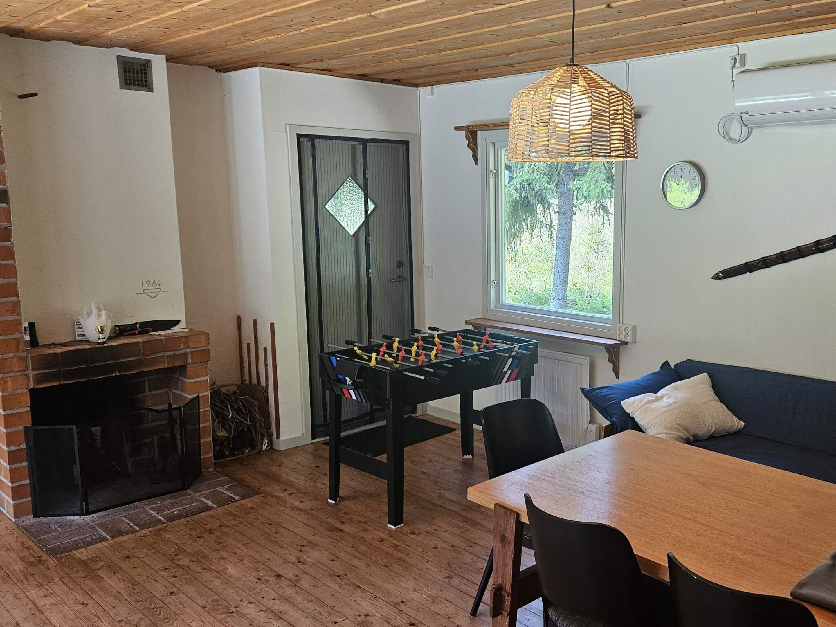 A cozy room with a foosball table, a brick fireplace, and a window with a view of trees.