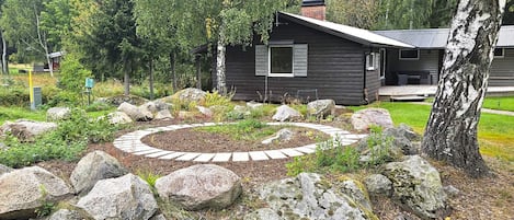 A cabin with a stone pathway leading to the entrance, surrounded by rocks and trees.
