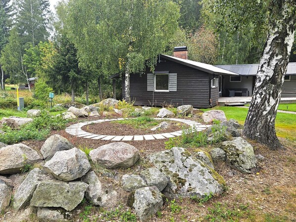 A cabin with a stone pathway leading to the entrance, surrounded by rocks and trees.
