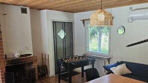 A cozy room with a foosball table, a brick fireplace, and a window with a view of trees.