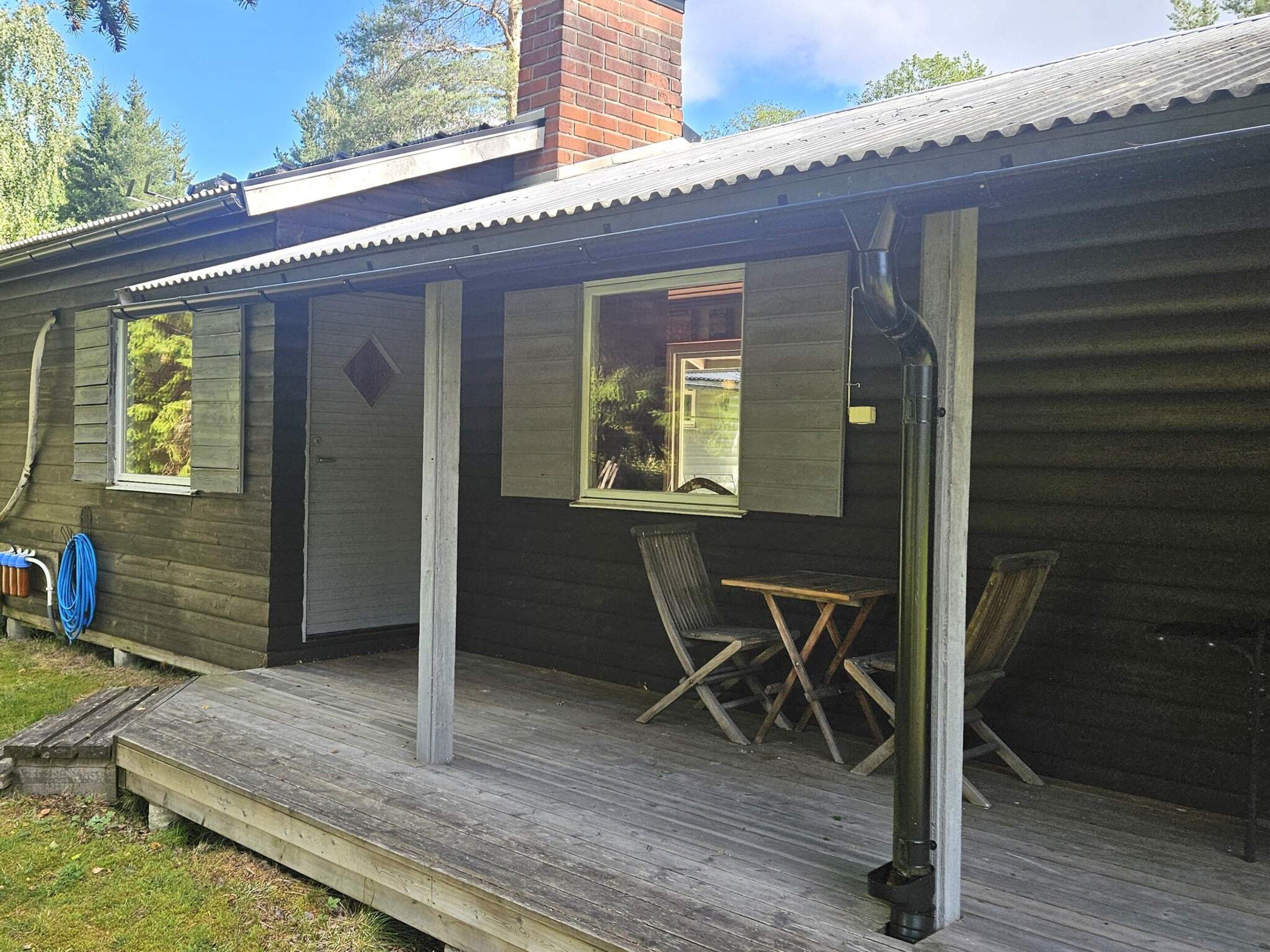 A wooden cabin with a porch, two windows, and a small table.