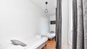 Een kleine, moderne kamer met twee eenpersoonsbedden, een houten vloer, een tv aan de muur en een hanglamp.