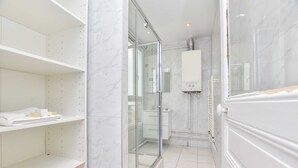 Een moderne badkamer met een douchecabine van glas, witte marmeren wanden en een ingebouwd plankje met handdoeken.