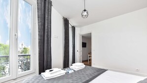 Een slaapkamer met een bed, een raam met gordijnen, een deur en een hanglamp.