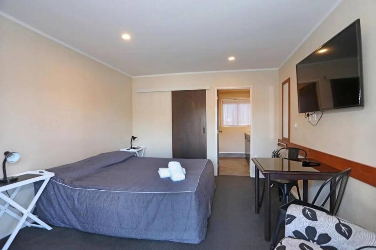 A hotel room with a bed, a desk, a chair, a TV, and a door leading to a bathroom.