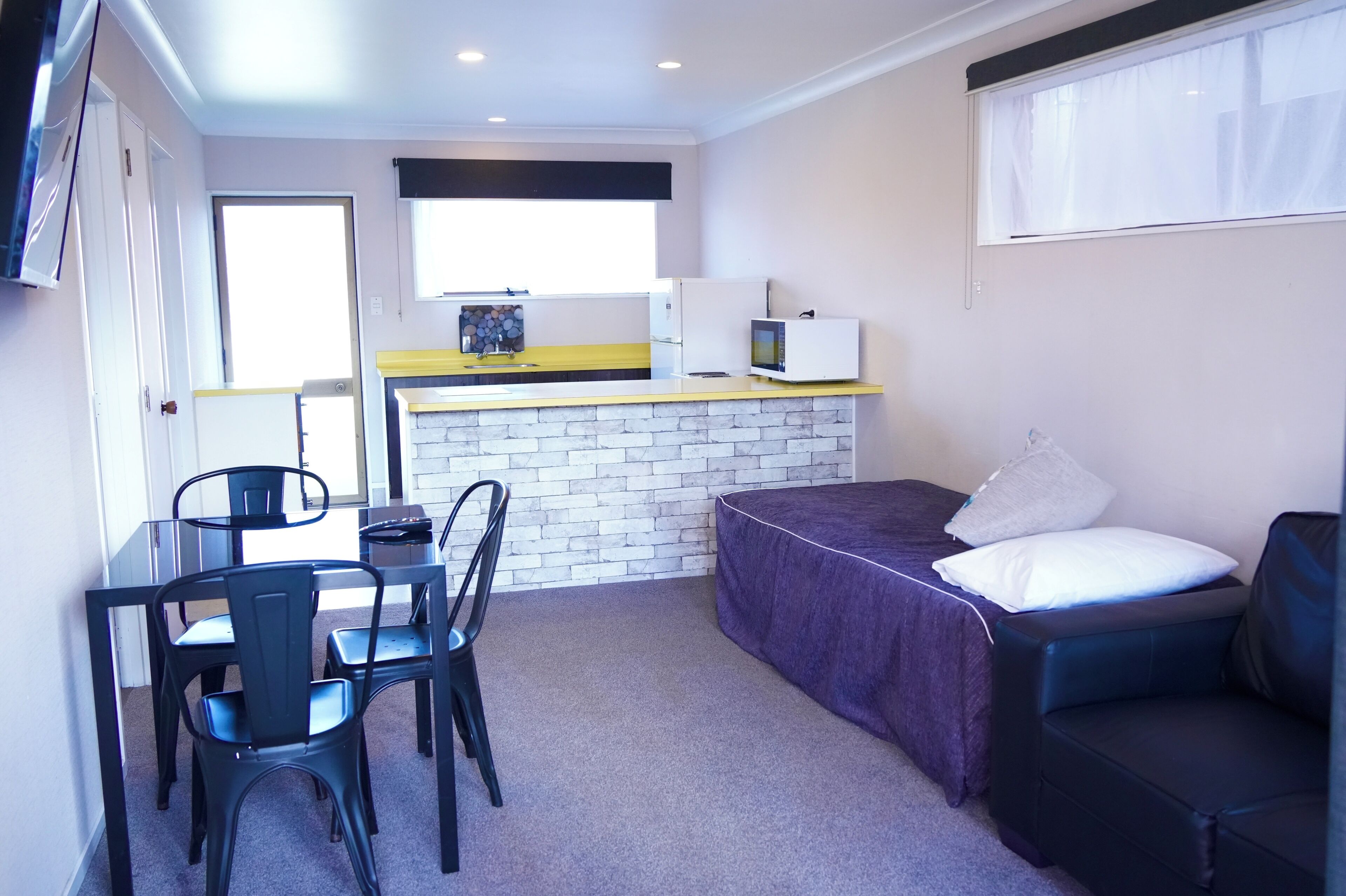 Una habitación compacta con cama, una pequeña mesa con sillas, kitchenette y una ventana.