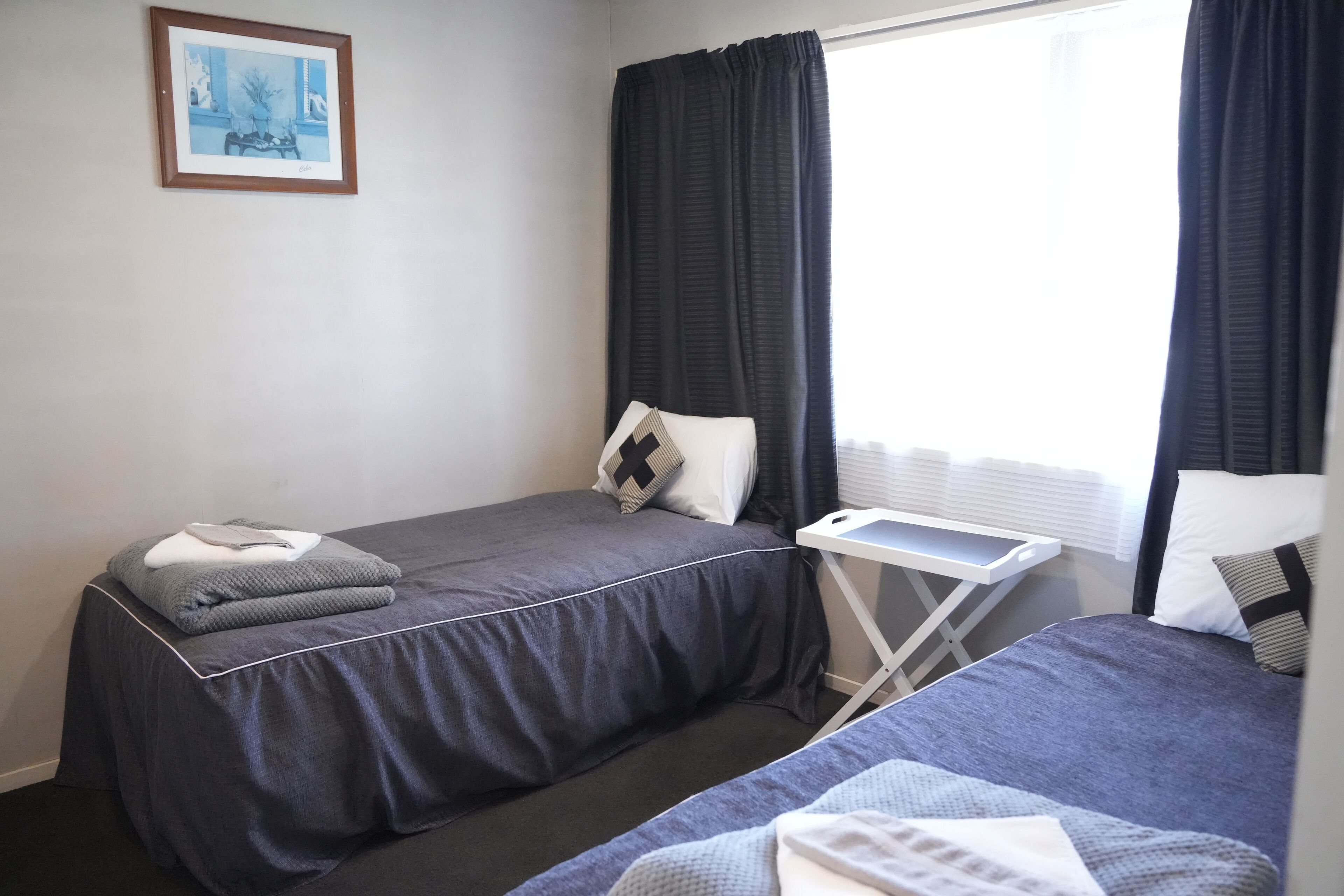 Une chambre avec deux lits, une petite table et une fenêtre avec des rideaux.