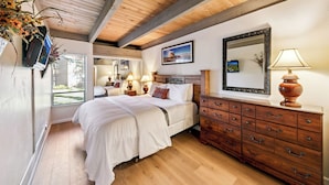 Une chambre avec un plafond en bois, un grand lit, une commode et un miroir.