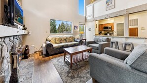 A cozy living room with a stone fireplace, a large TV, and a sofa. There's a kitchen area with a microwave and a coffee machine.