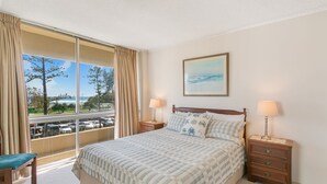 Una habitación de hotel con un ventanal grande, una cama con colcha a rayas, dos mesitas de noche con lámparas, y un cuadro en la pared.
