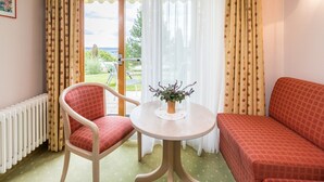 A room with a red sofa, a chair, a small table with a plant, and a view of the outdoors through a door. - Room 'Doppelzimmer 3' with Mountain View, Private Terrace and Wi-Fi (Gailingen am Hochrhein)