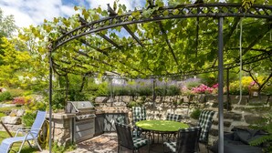 Eine überdachte Terrasse im Freien mit Grill, Esstisch und Stühlen.