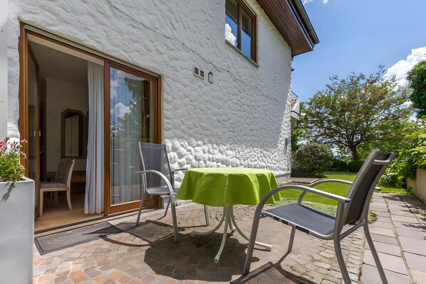 Un patio con una mesa y sillas, una pared blanca con textura y una puerta que da a un espacio interior.