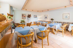 Un restaurante con varias mesas y sillas, una zona de recepción y obras de arte en las paredes.