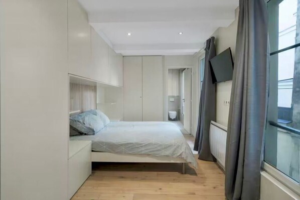 A modern bedroom with a bed, built-in wardrobe, and a TV on the wall. - Le Marais • Charm & Comfort (Paris)