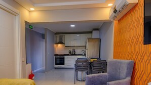 A modern hotel room with a dining area, kitchenette, and a TV mounted on the wall.