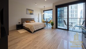 A modern bedroom with a large bed, a desk, and a balcony with a city view. - Towarowa Towers Residences (Warsaw)