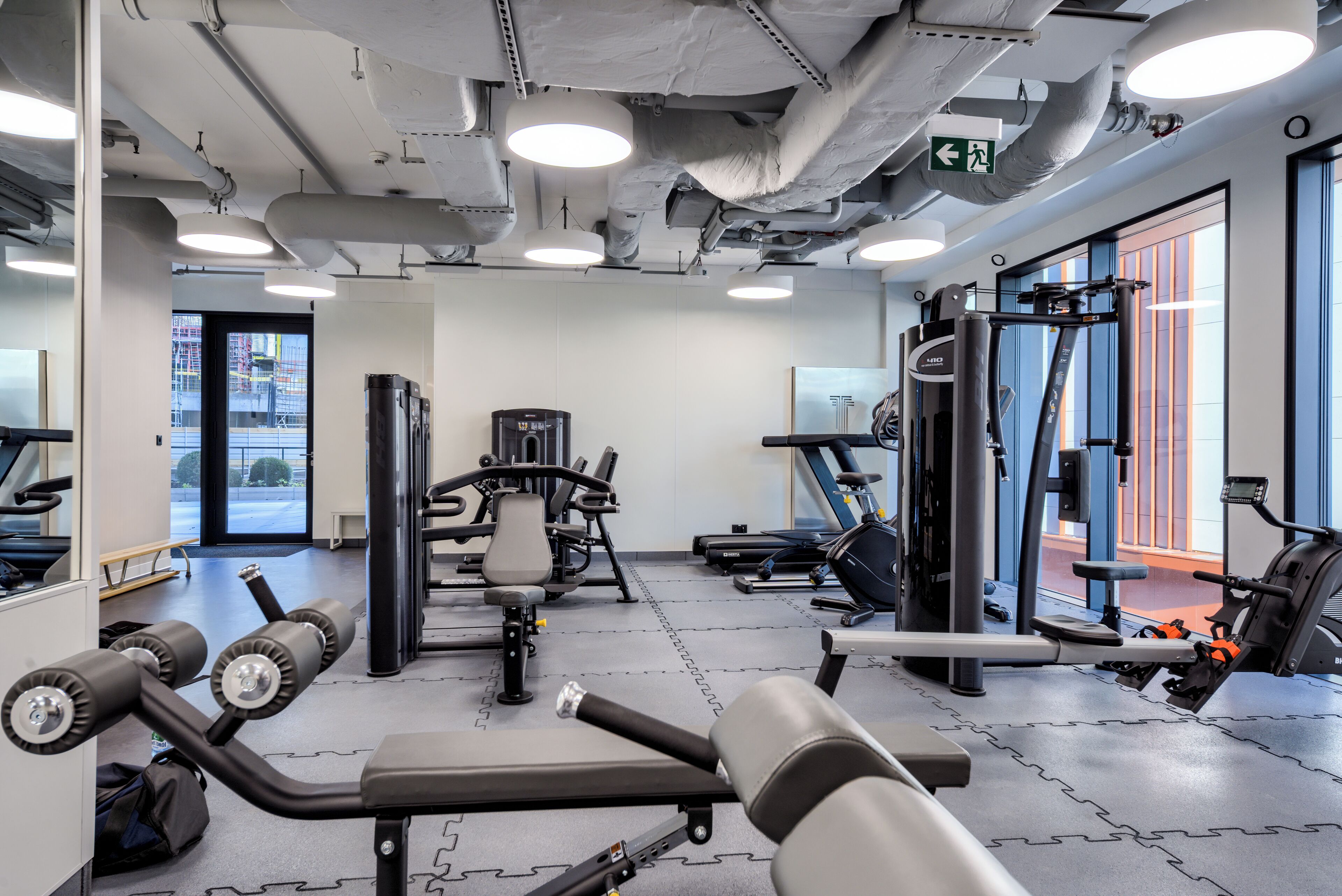 Ein Fitnessraum mit Trainingsgeräten, einem Spiegel und einer Tür, die nach draußen führt.