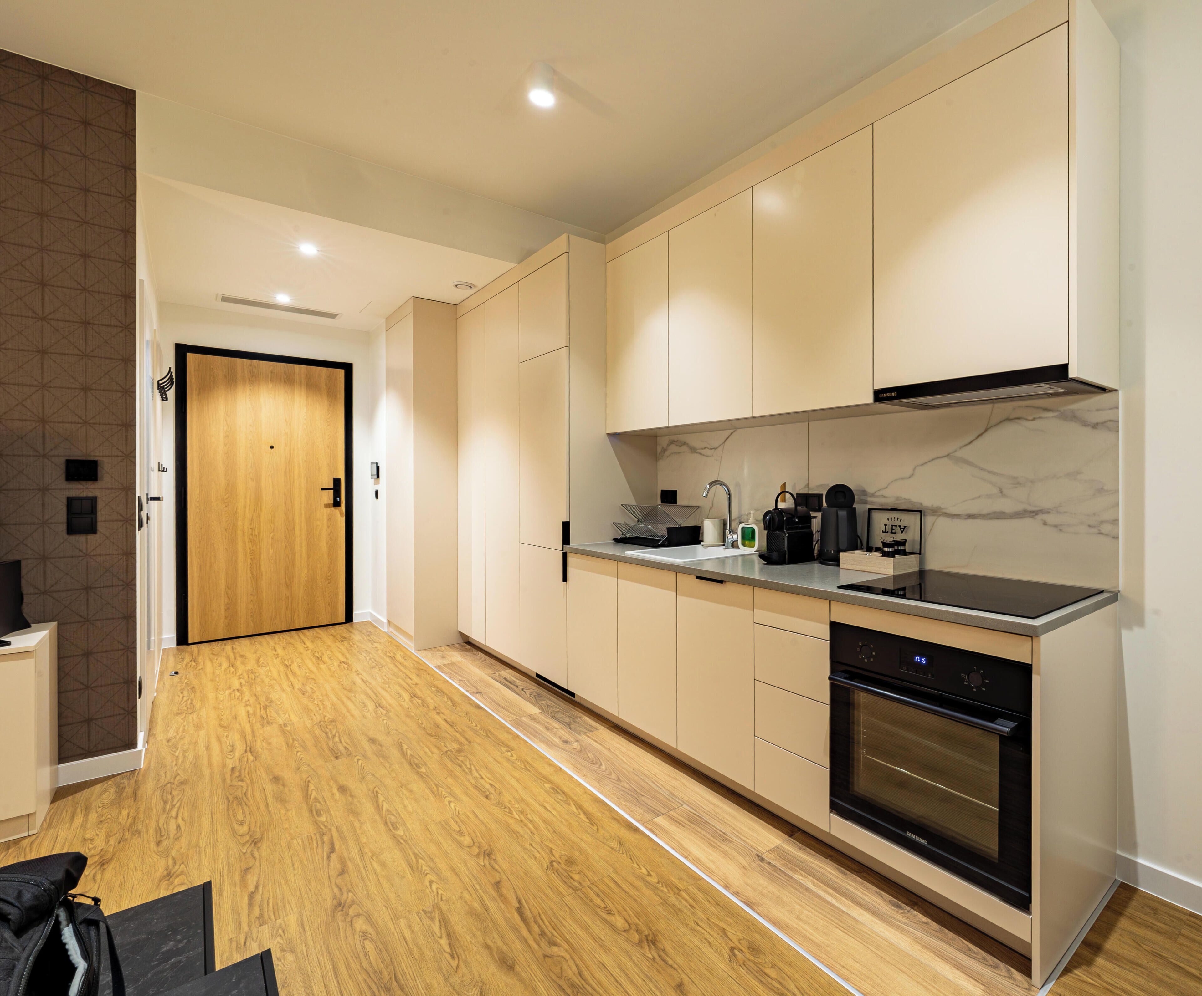 A modern kitchen with wooden flooring, a built-in oven, and a marble backsplash.