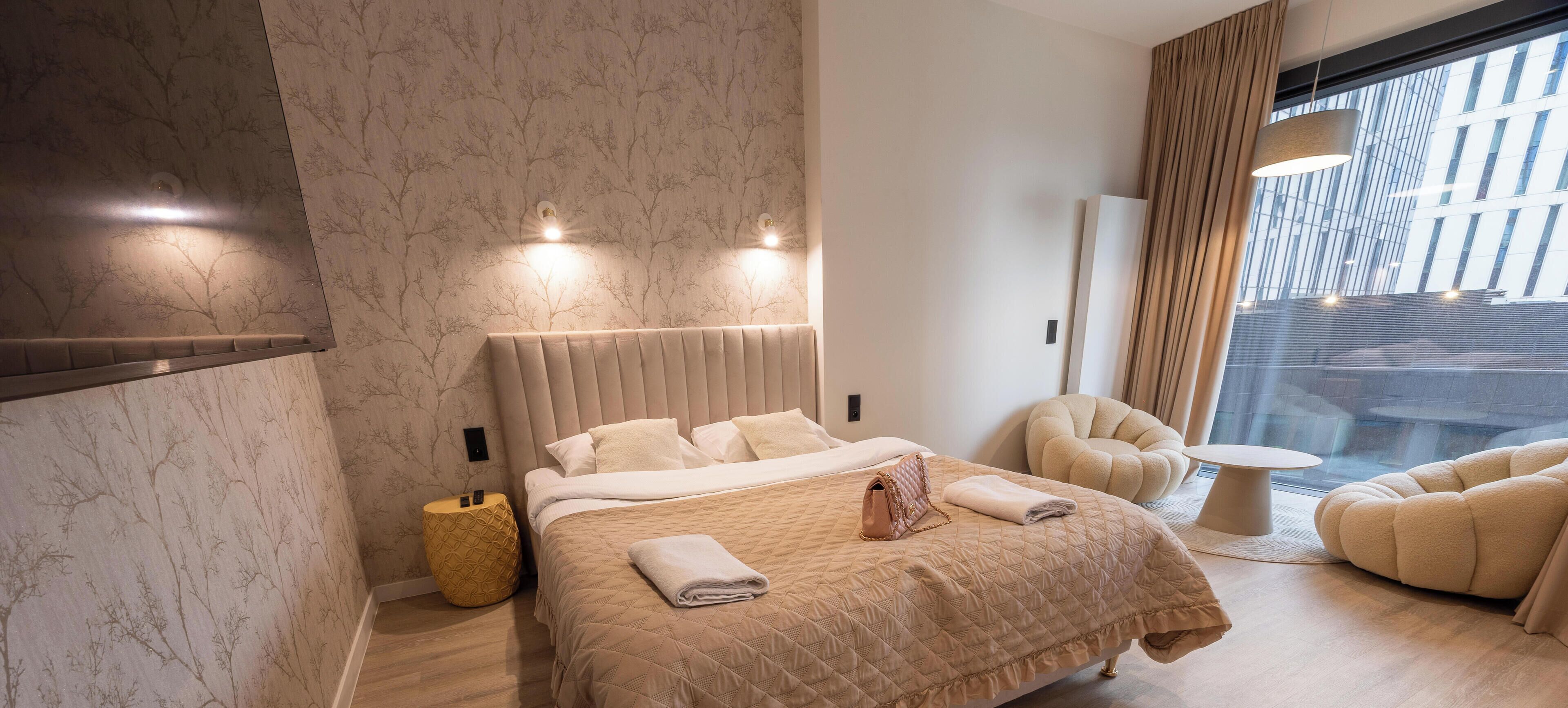 Ein modernes Hotelzimmer mit einem großen Bett, einer Sitzecke und Blick auf die Stadt durch das Fenster.