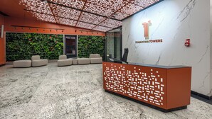 A reception area with a modern design, featuring a marble wall, a logo, and a seating area with plants. - Towarowa Towers Residences (Warsaw)