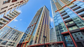 A modern high-rise building with a glass facade and red accents, surrounded by other tall buildings. - Towarowa Towers Residences (Warsaw)