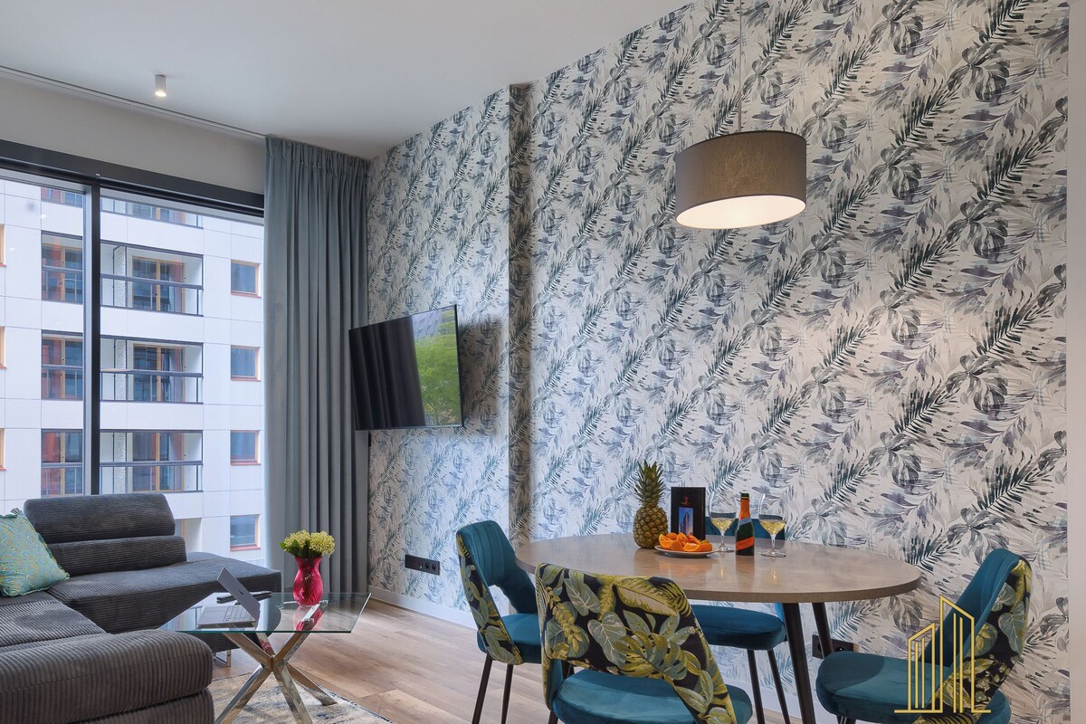 Una sala de estar moderna con un sofá gris, sillas azules, una mesa de comedor de madera y un papel tapiz estampado.